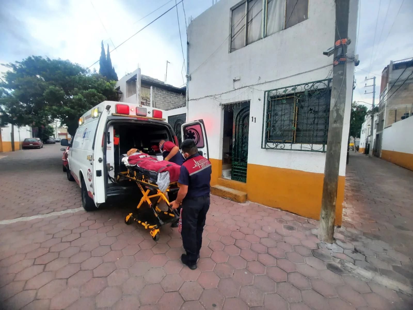 Paramédico realizando traslado de paciente en camilla desde domicilio